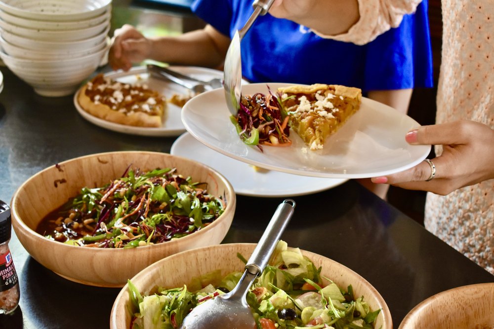 Slice of seasonal tart being served with bowls of fresh salads