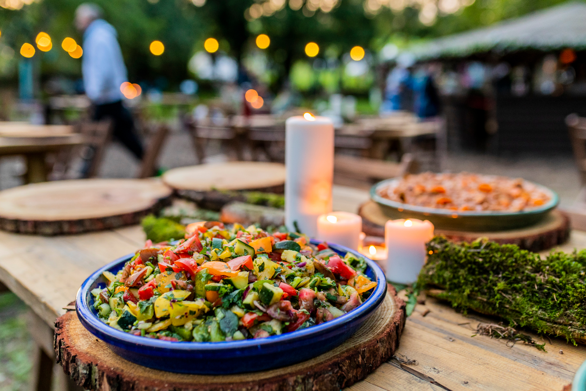 Long-table salad bowl by candlelight under festoon lights in the woods