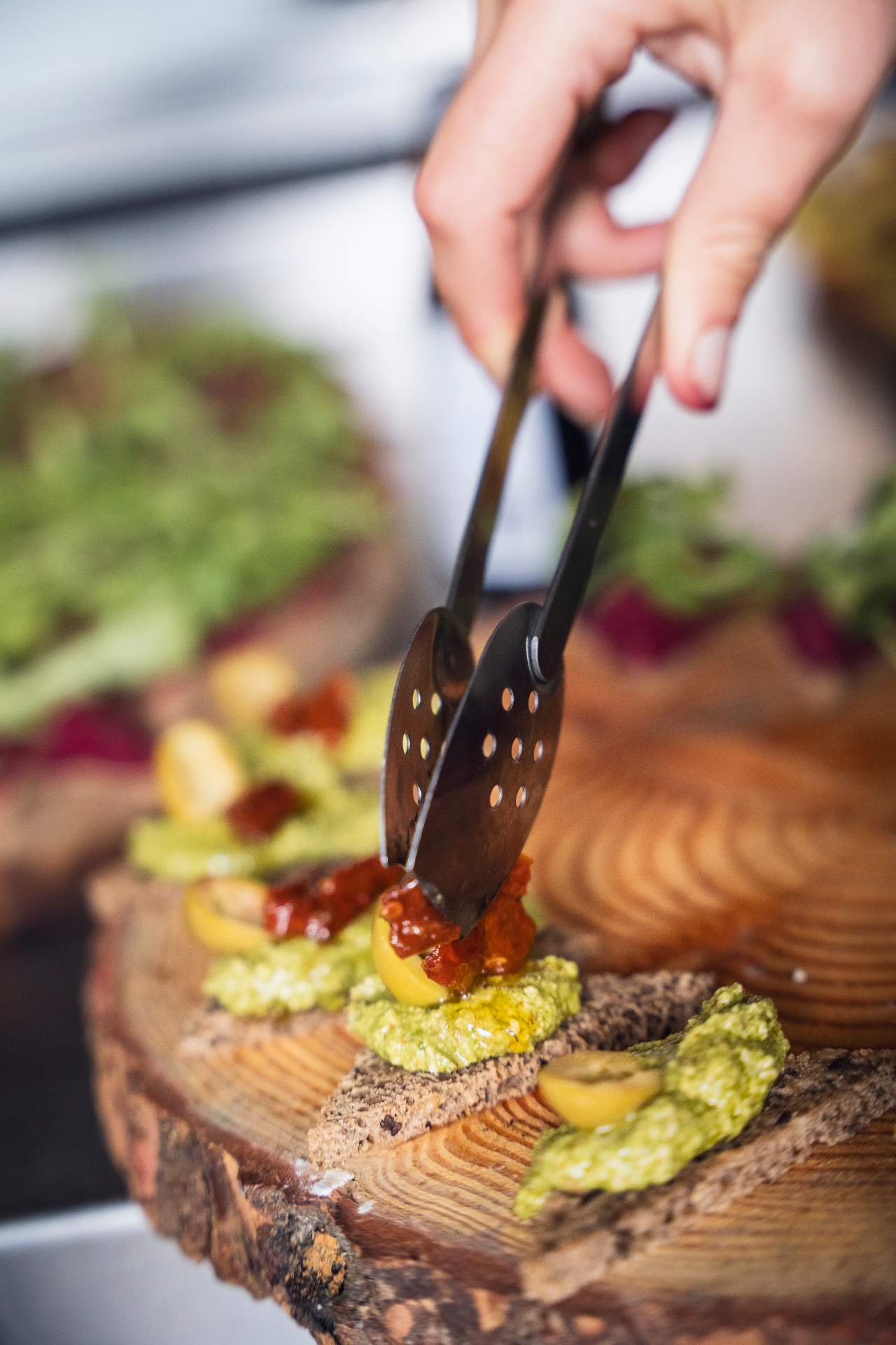Chef plating canapés with pesto and tomato on a wooden round