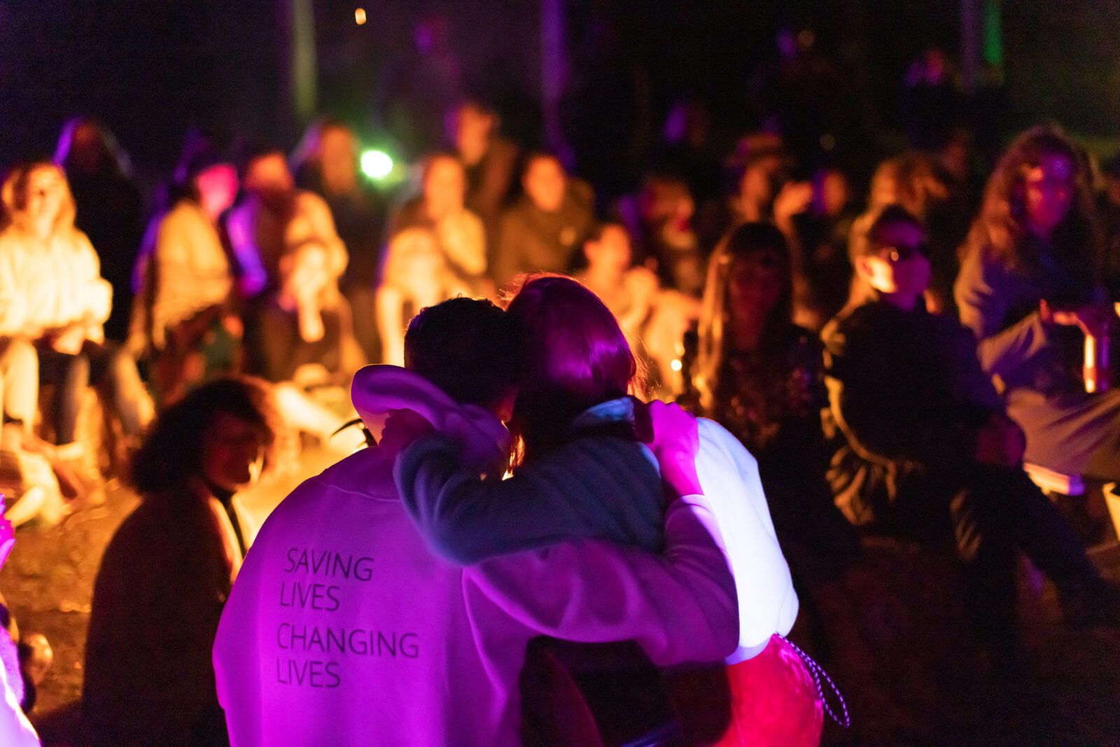 Two festival-goers embracing in the firelight at night