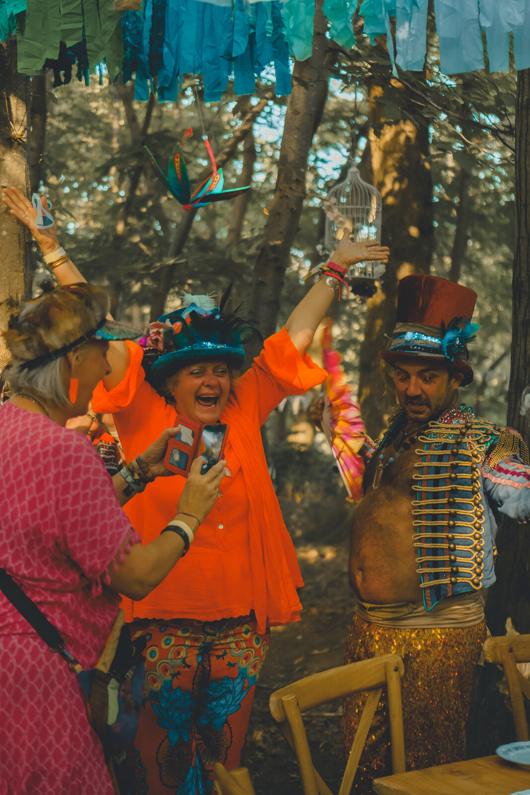 Festival-goers in orange costumes and top hats laughing in the woods