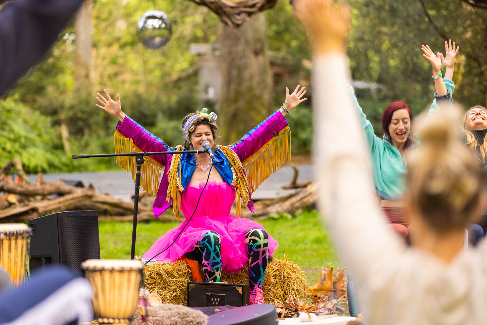 Singer in pink and gold fringe with arms raised on the woodland stage